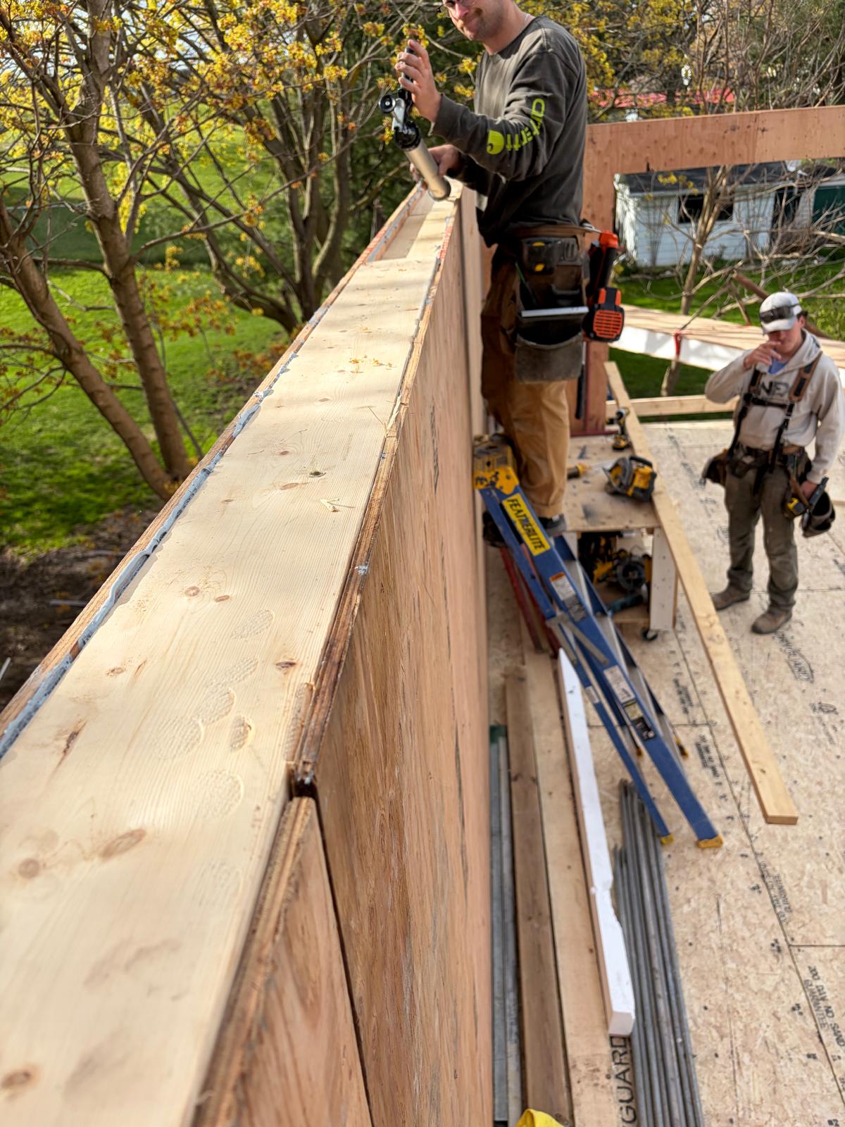 Worker on roof fastening ridge beam of SIP panel home with drill